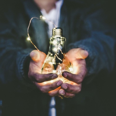 A pair of hands holding an illuminated light bulb